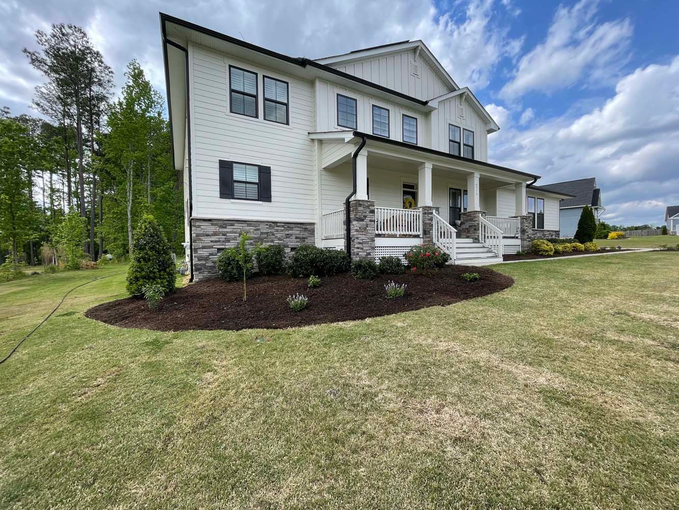 A large white house with a large porch is sitting on top of a lush green field.