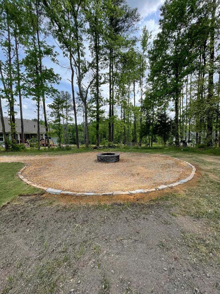 A fire pit in the middle of a dirt field surrounded by trees.