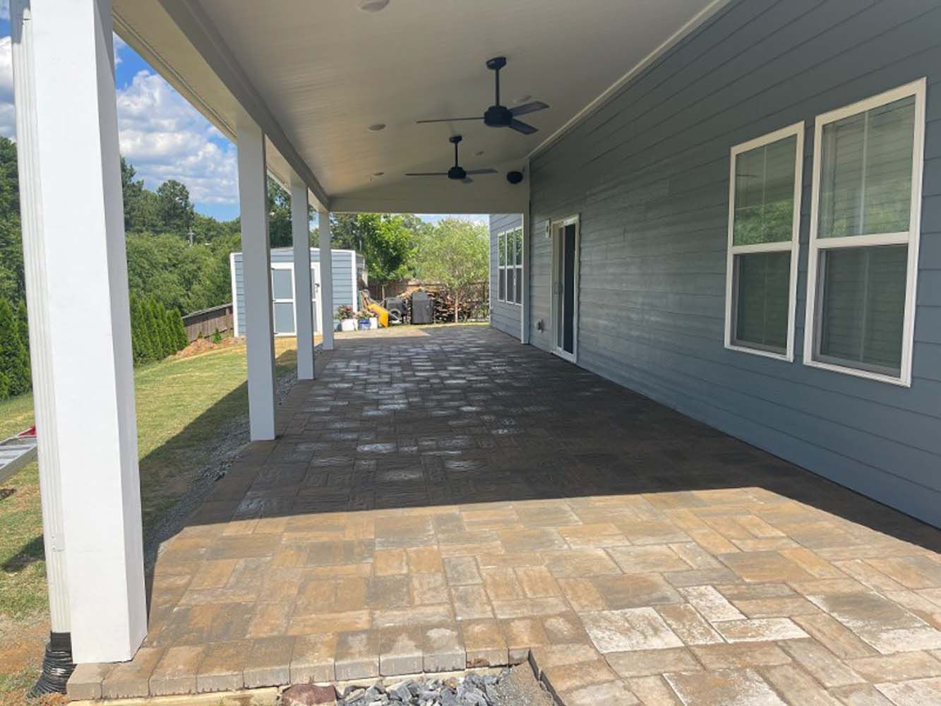A large covered patio with a ceiling fan in the backyard of a house.