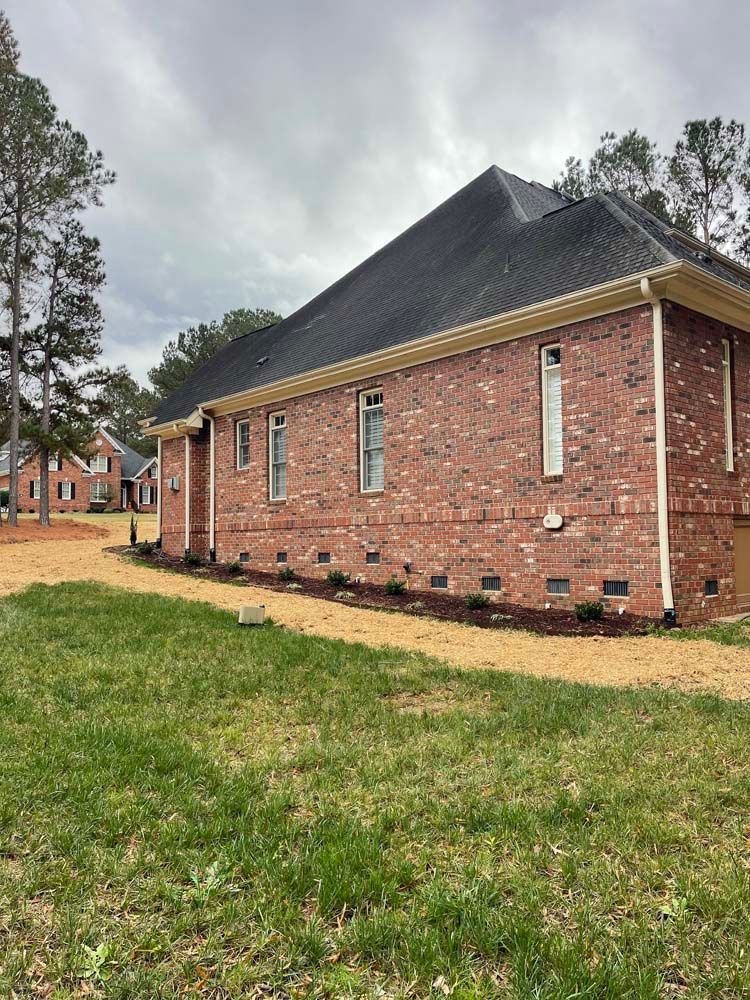 A brick house with a black roof is sitting on top of a lush green field.