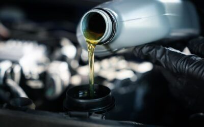Motor oil pouring from a bottle into an engine oil cap under the hood
