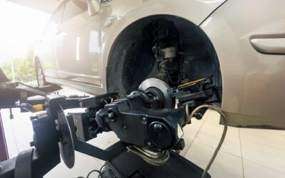 Car suspended on a wheel alignment rack with front wheel removed, showing brake and suspension components