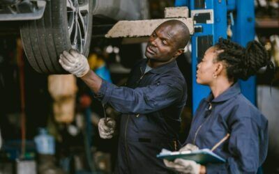 Mechanic inspecting a large tire while a colleague observes in a workshop