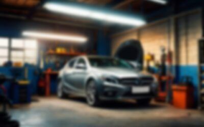 Silver car in a garage with its hood open, under bright shop lights