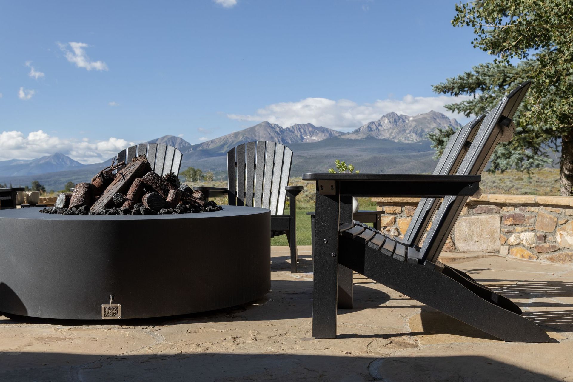Black recycled plastic Adirondack chairs around a fire pit with mountain backdrop.