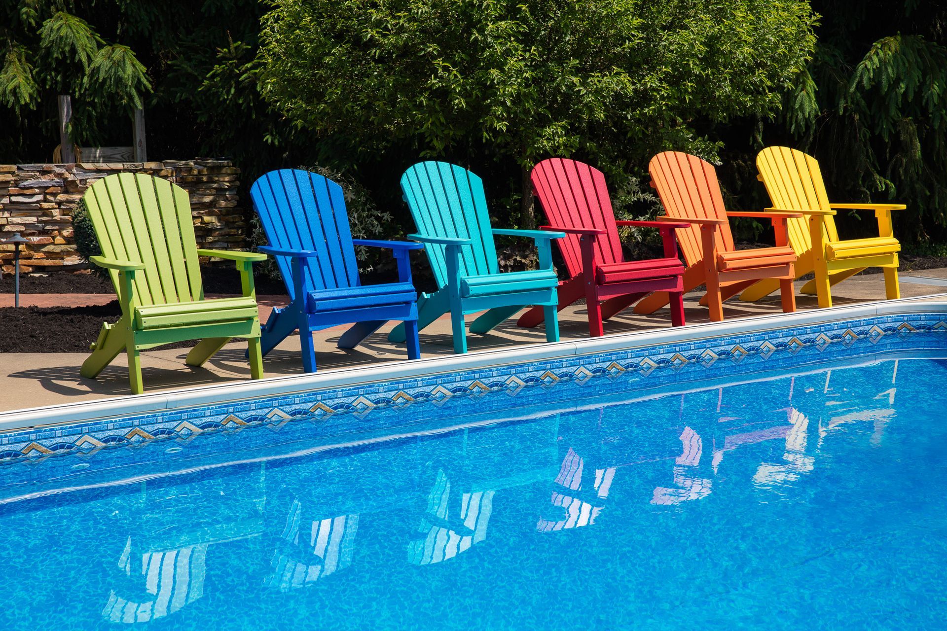 Comfo-Back Folding Adirondack chairs in bright tropical colors lined up along the edge of a pool at a Lewisburg, Pennsylvania home.