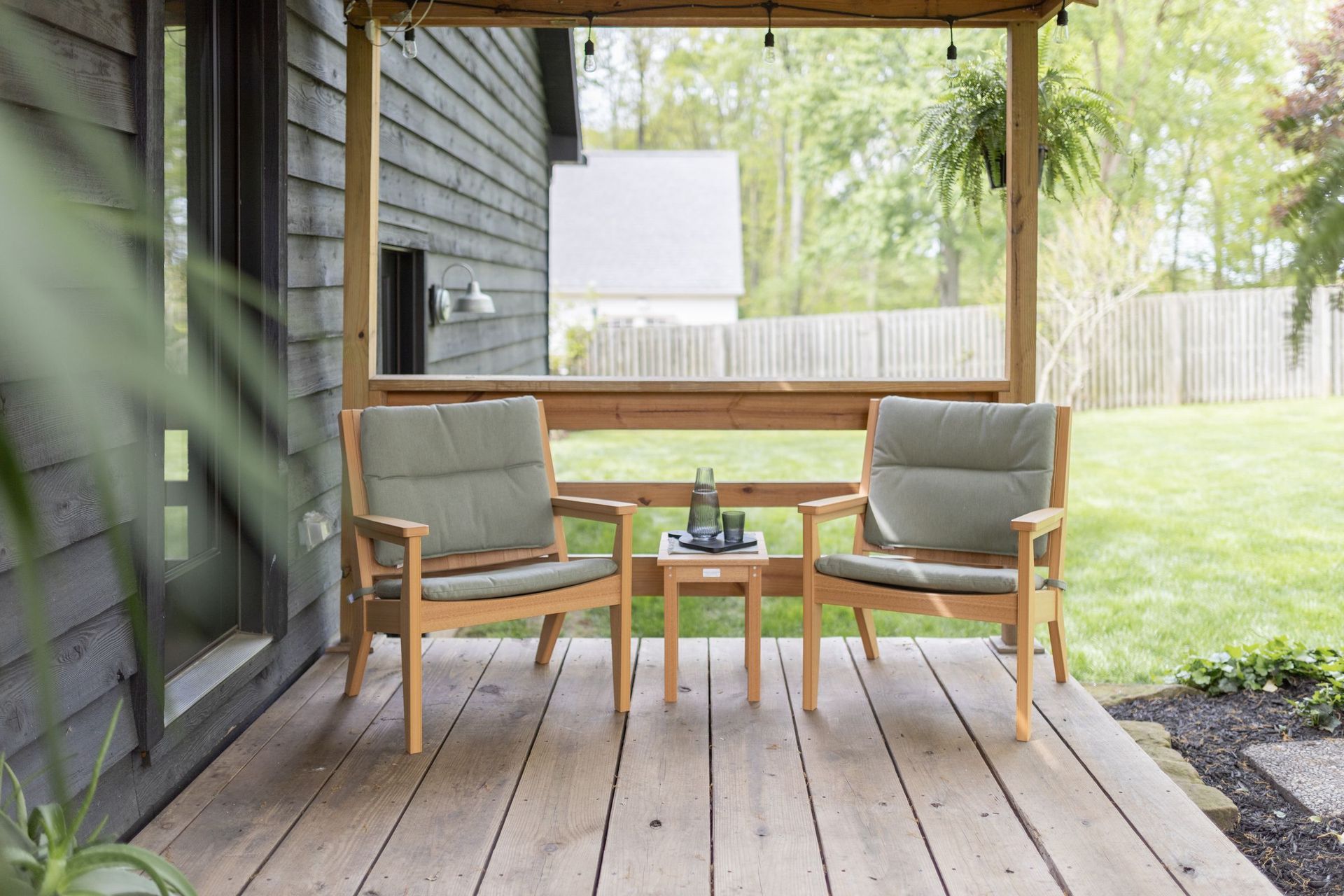 Mayhew Chat chairs and HDPE recycled plastic end table in Natural Teak with green Heritage Leaf cushions on a front porch.