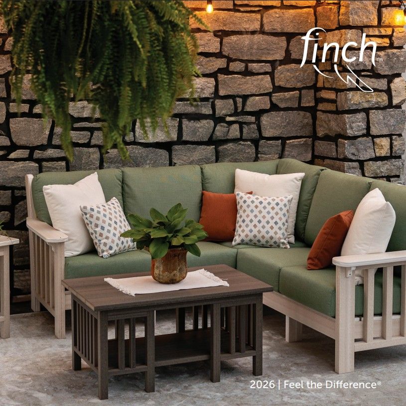 Outdoor patio seating with green sectional, white pillows, wooden table, and stone wall backdrop