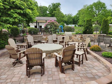 Patio with fire pit, surrounded by chairs, trees, and stone wall.