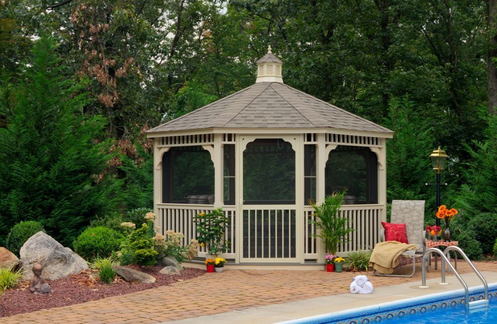Beige gazebo by a pool, screened windows, surrounded by greenery and a brick patio.
