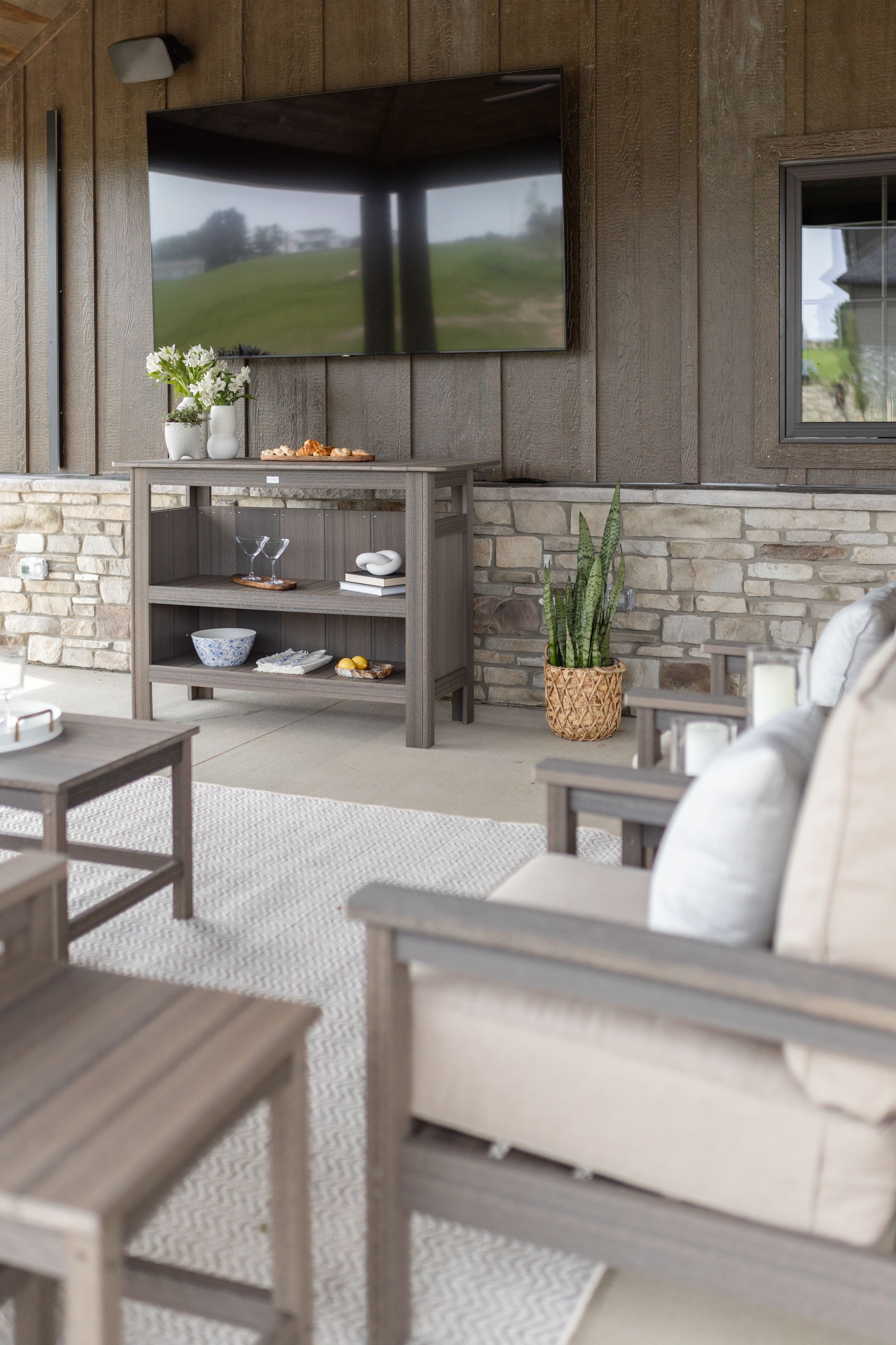 Outdoor seating area with a TV, bar, and stone wall.