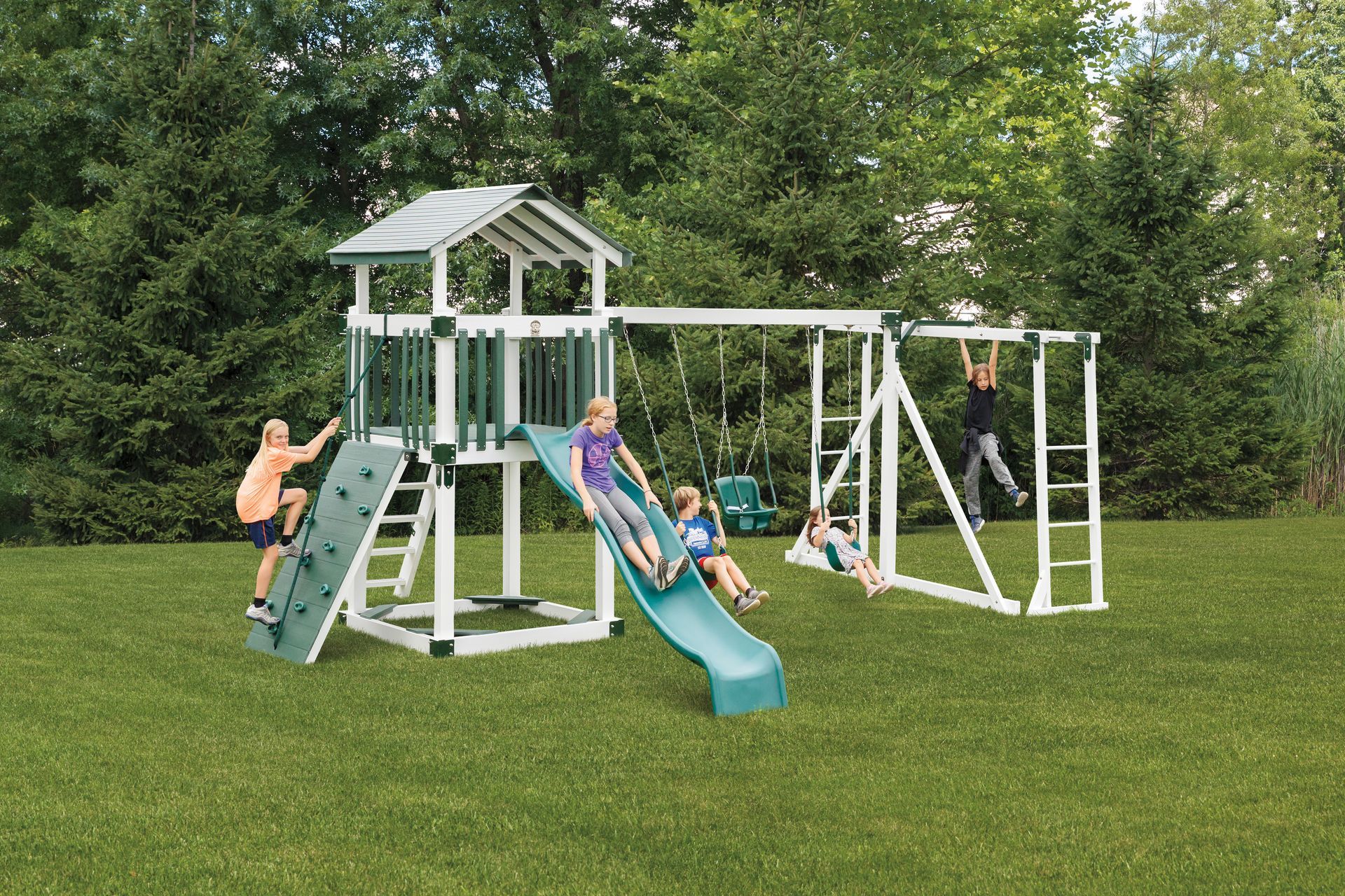 Children playing on a green and white playset in a grassy yard.
