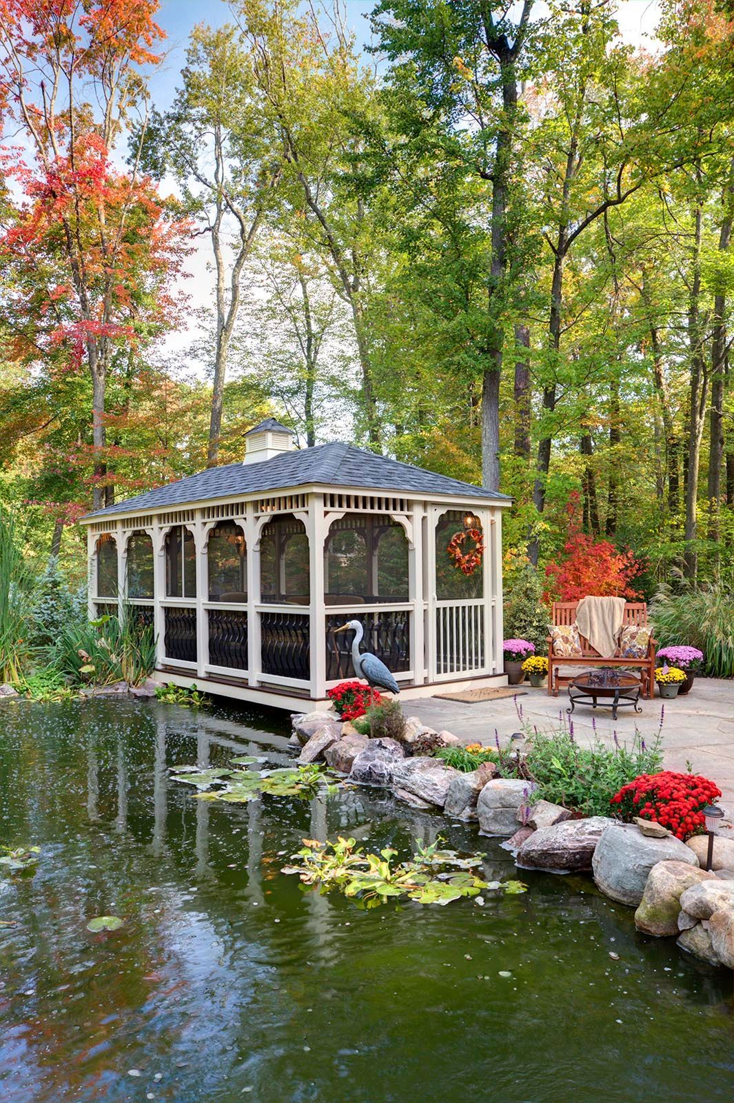 Gazebo over pond surrounded by trees, with colorful autumn foliage.