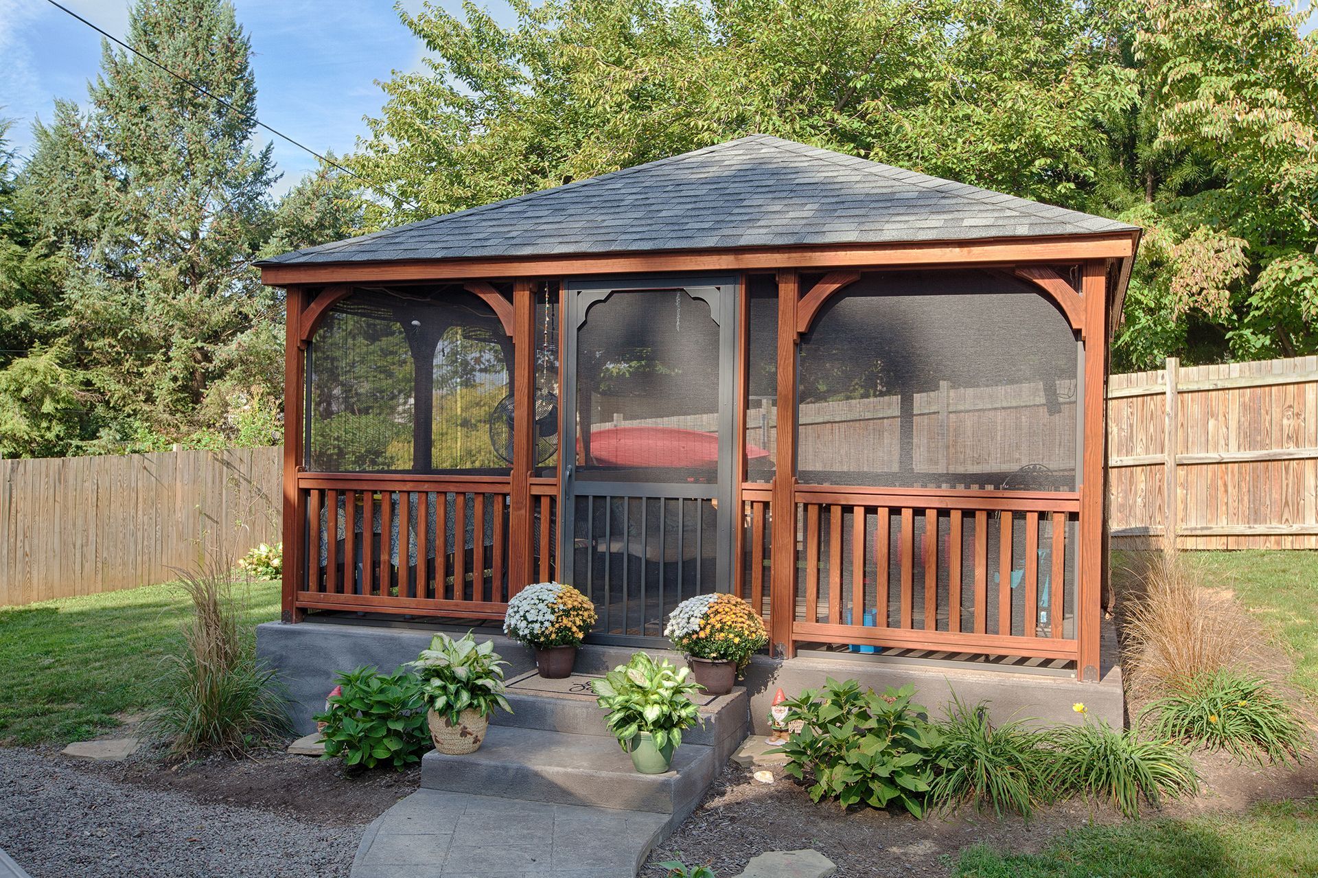 Screened wooden gazebo with a brown roof and a small stone step in a yard.