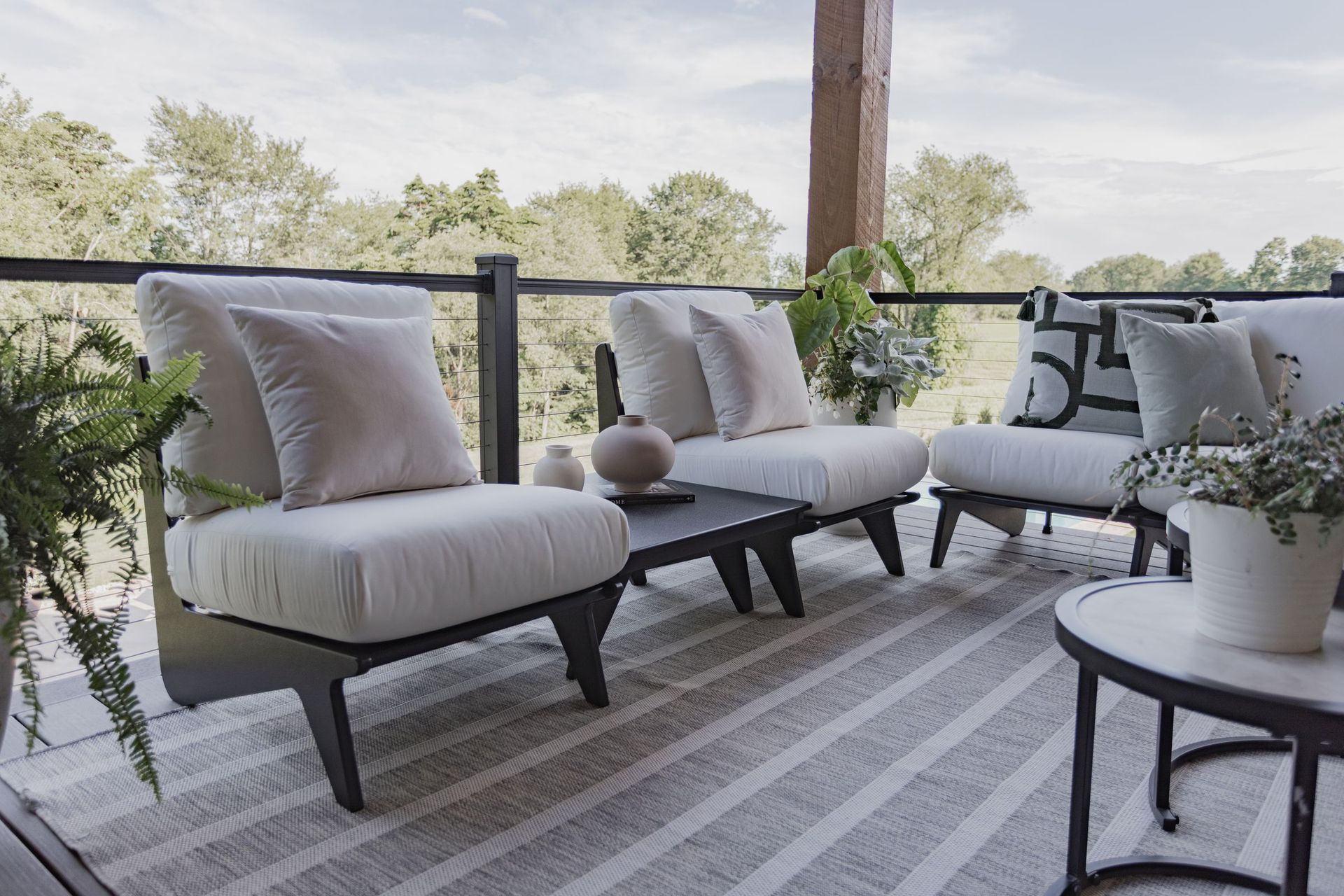 Outdoor seating area with gray chairs, rug, and coffee table on a deck overlooking trees.