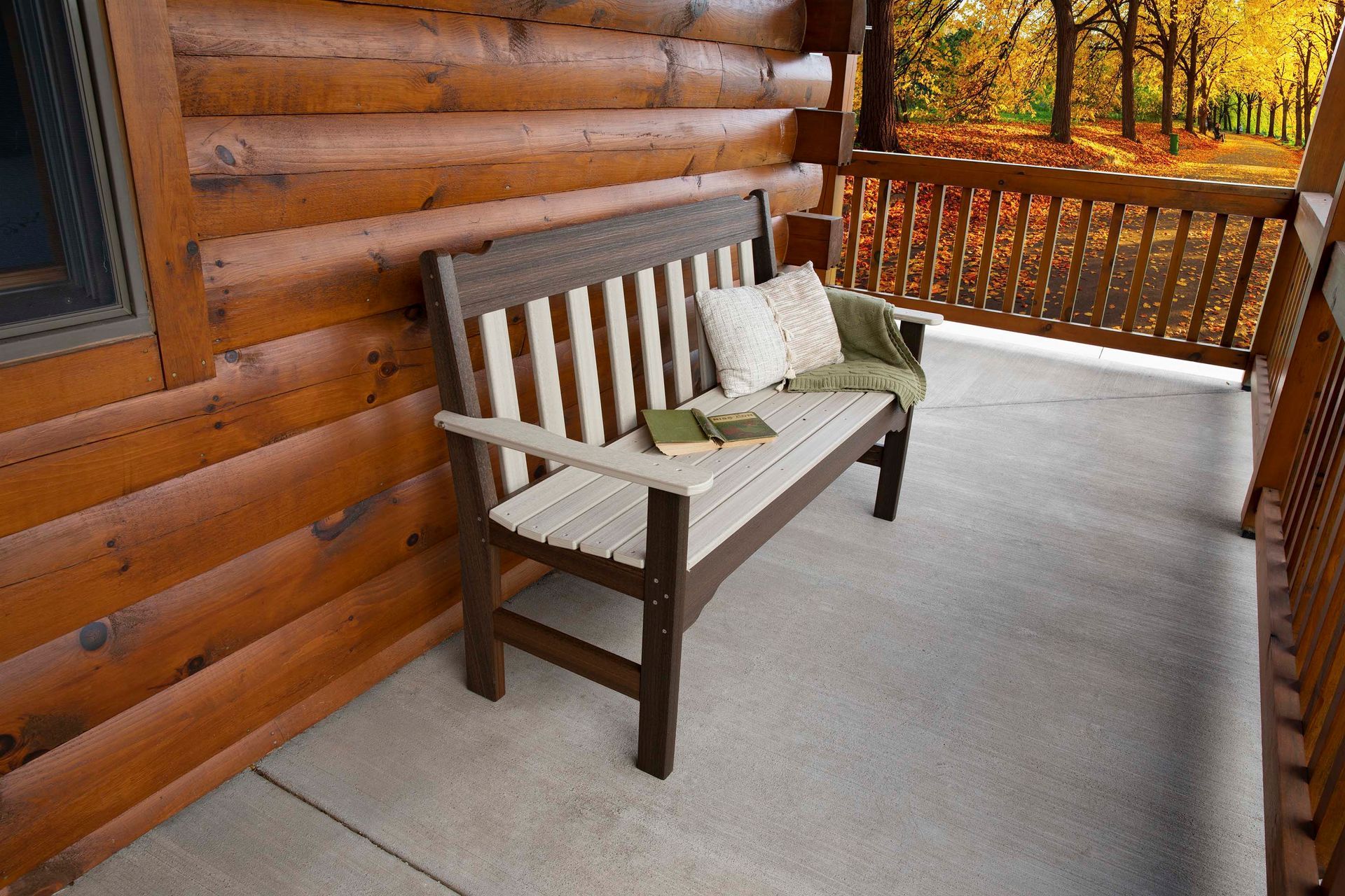 A wooden bench with cushions and a book on a porch of a log cabin, with an autumn forest view.