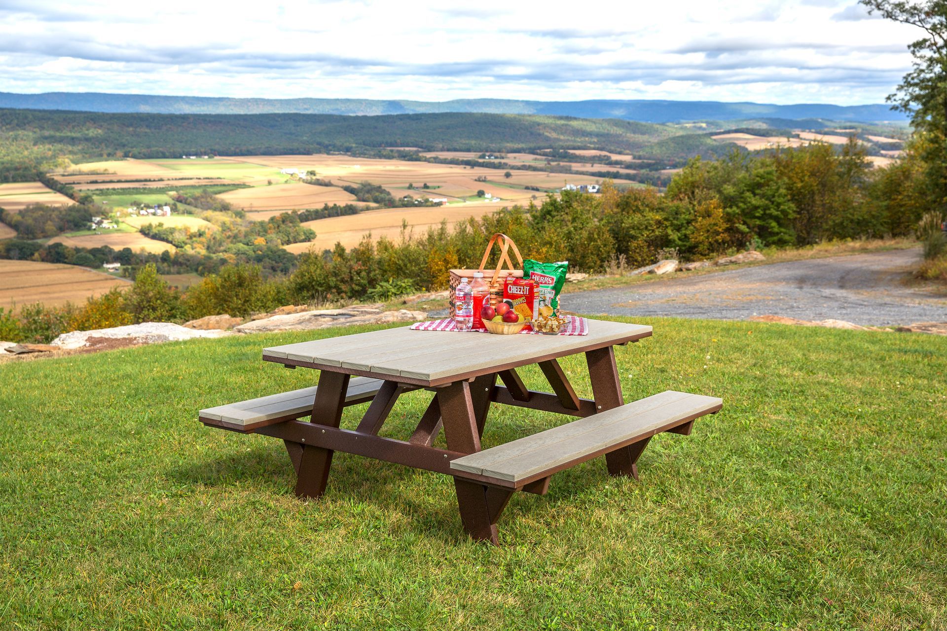 Picnic table on a grassy hilltop overlooking a valley, with food and a scenic background.
