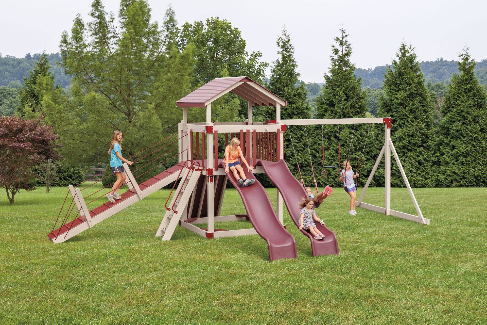 Children playing on a wooden playground set with swings, slides, and a climbing ramp.