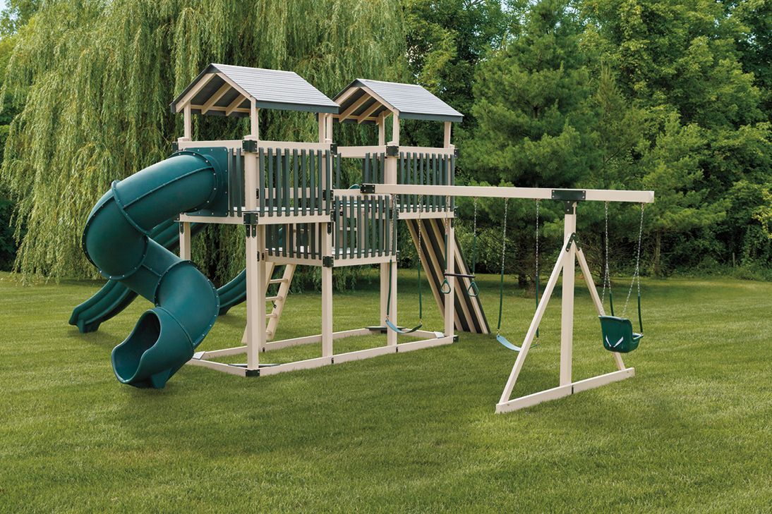 Playset on a grassy lawn with a green slide, swing set, and two wooden towers.