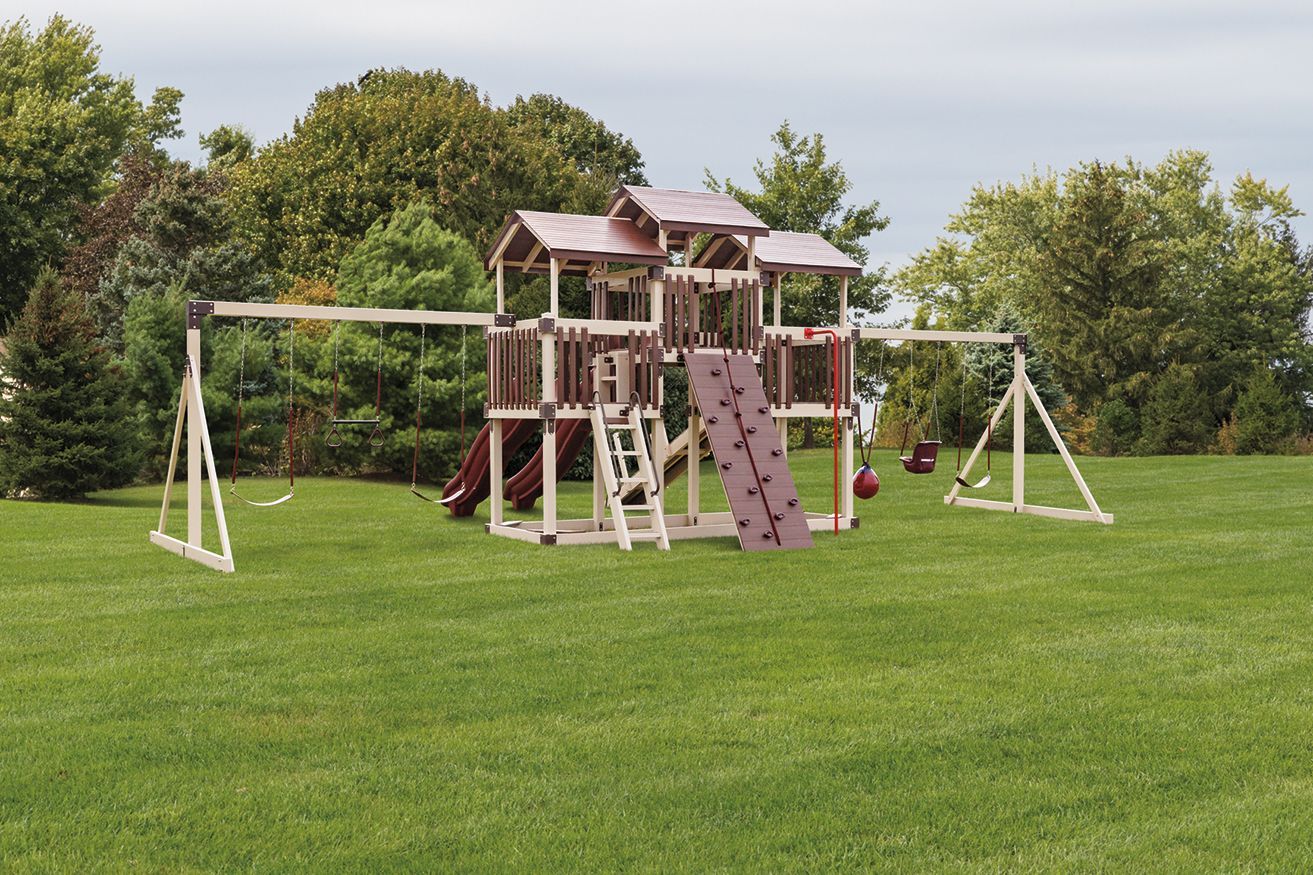 Wooden playset with swings, slide, climbing wall, and playhouse in a grassy yard.