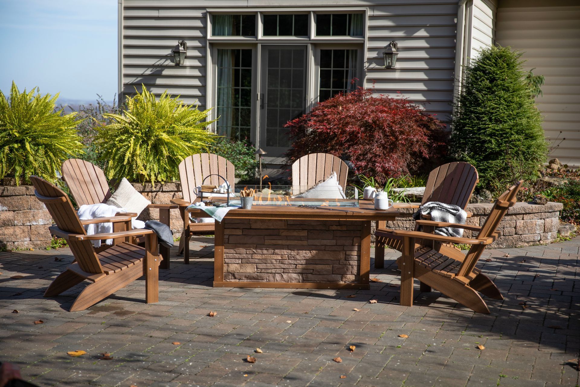 Patio seating area with Adirondack chairs around a fire pit, near a house.