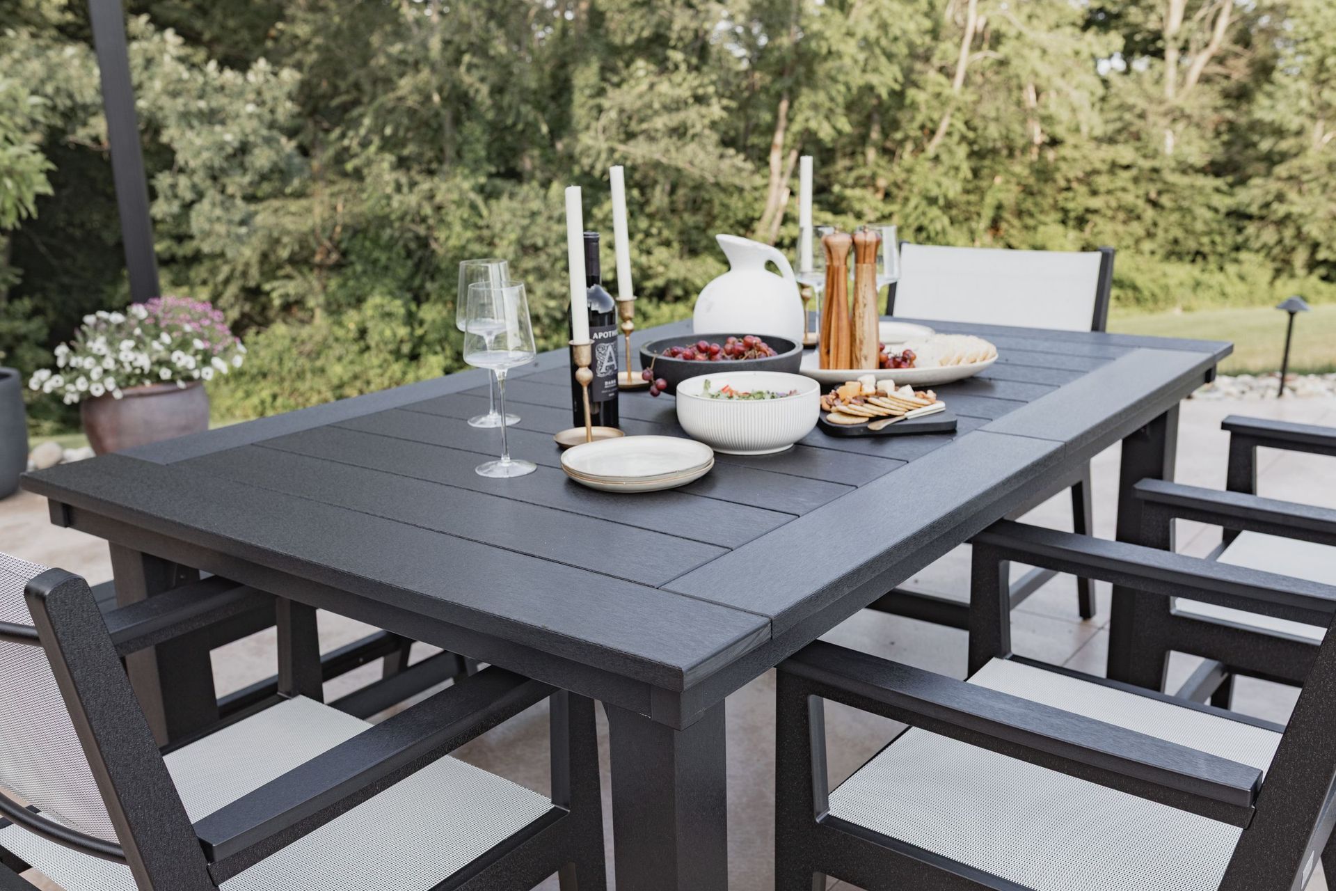 Outdoor dining table set with food and candles, set on a patio, overlooking trees.