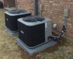 Two outdoor AC units on concrete pads next to a brick wall.