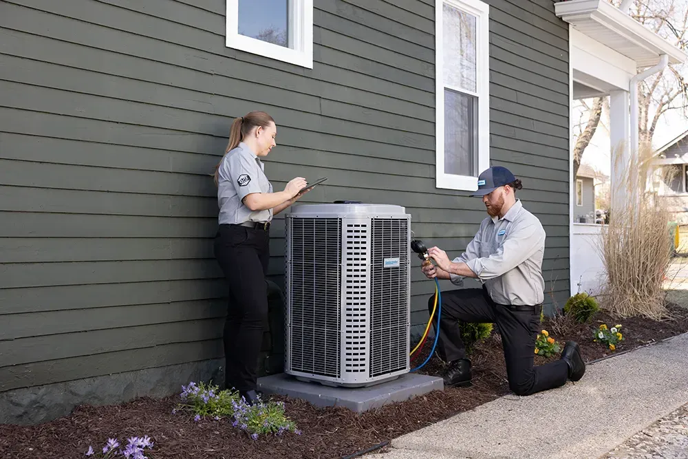 HVAC technician applying sealant to a furnace in a garage.