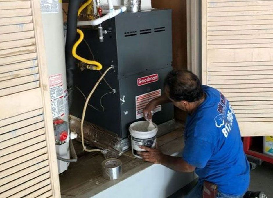 HVAC technician applying sealant to a furnace in a garage.