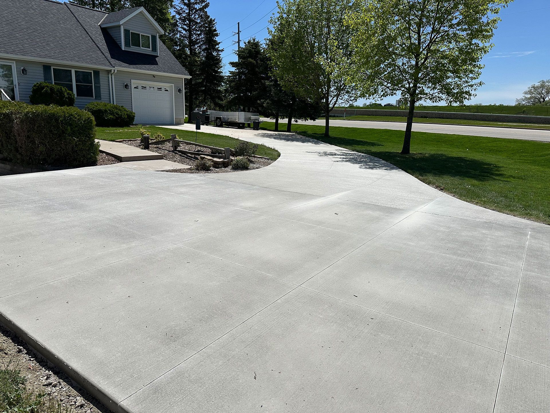 A concrete driveway leading to a house with trees in the background
