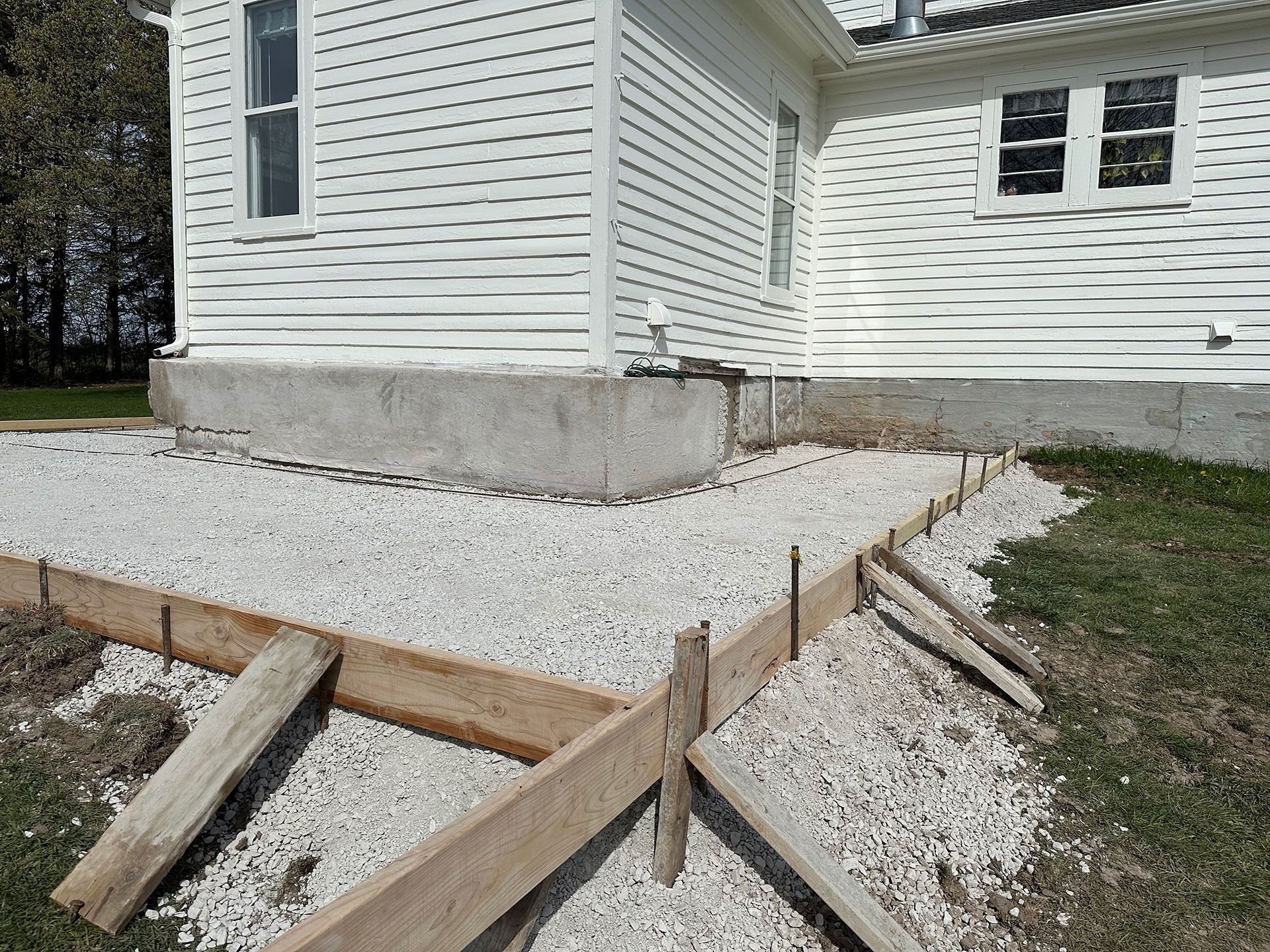 A white house is being remodeled, and a concrete walkway is being built in front of it