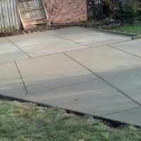 A concrete driveway in a backyard with a fence in the background.