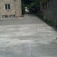 A concrete driveway leading to a house with a stone building in the background.