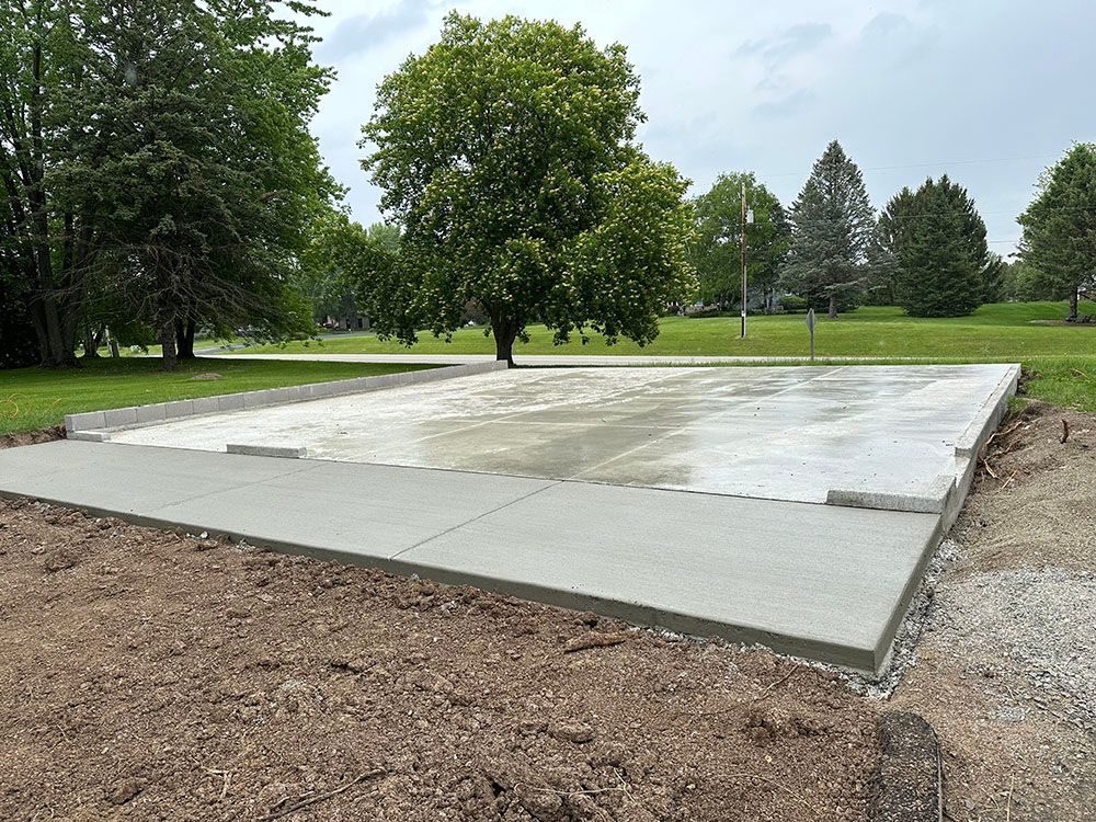 A concrete foundation is being built in a park with trees in the background.