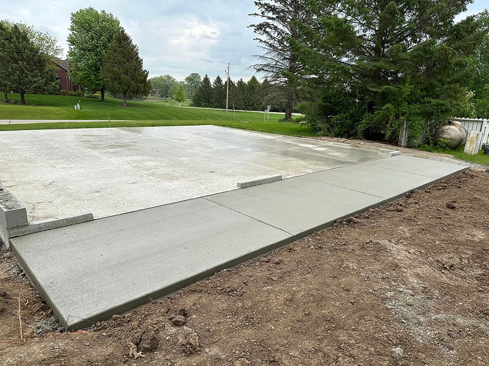 A concrete driveway is being built in a yard with trees in the background.