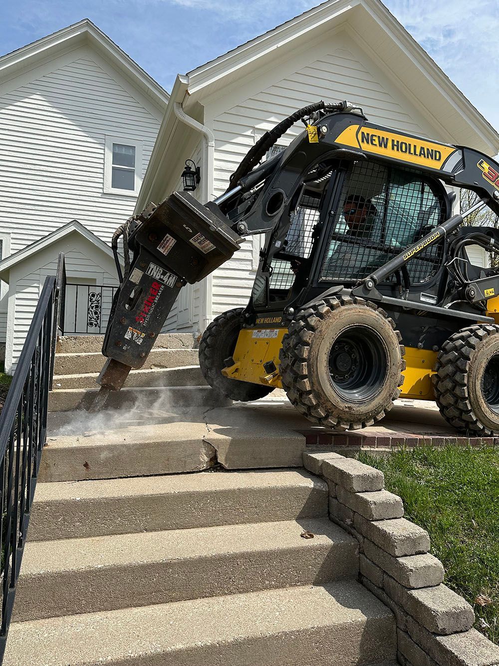 A bulldozer is cutting concrete steps in front of a house.
