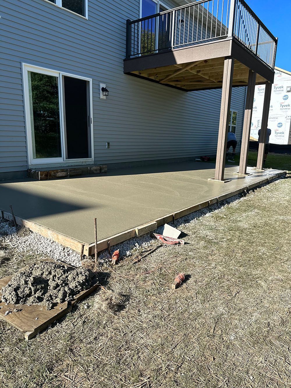 A concrete patio is being built in front of a house with a deck.