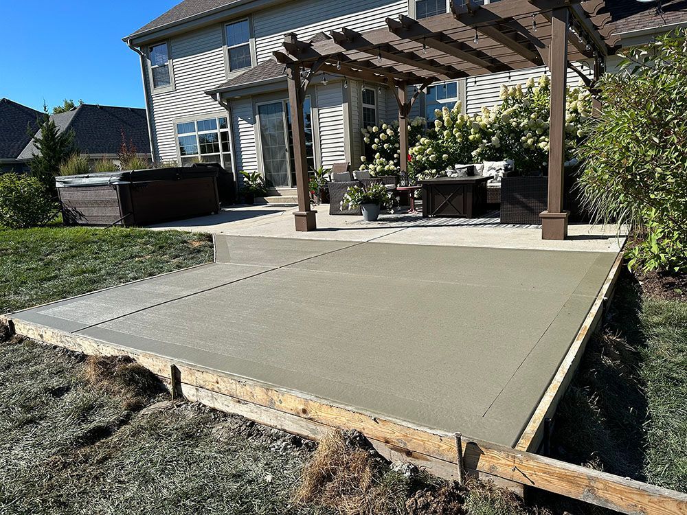 A concrete patio is being built in front of a house with a pergola.