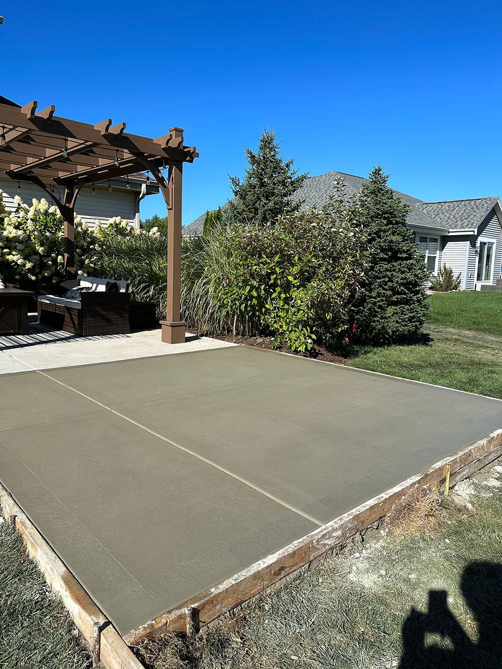 A concrete patio with a pergola and a house in the background.