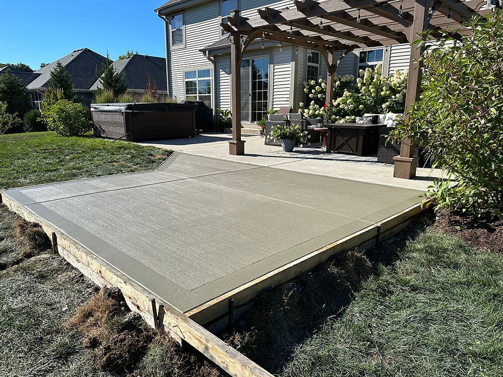A patio with a pergola and a hot tub in the background.