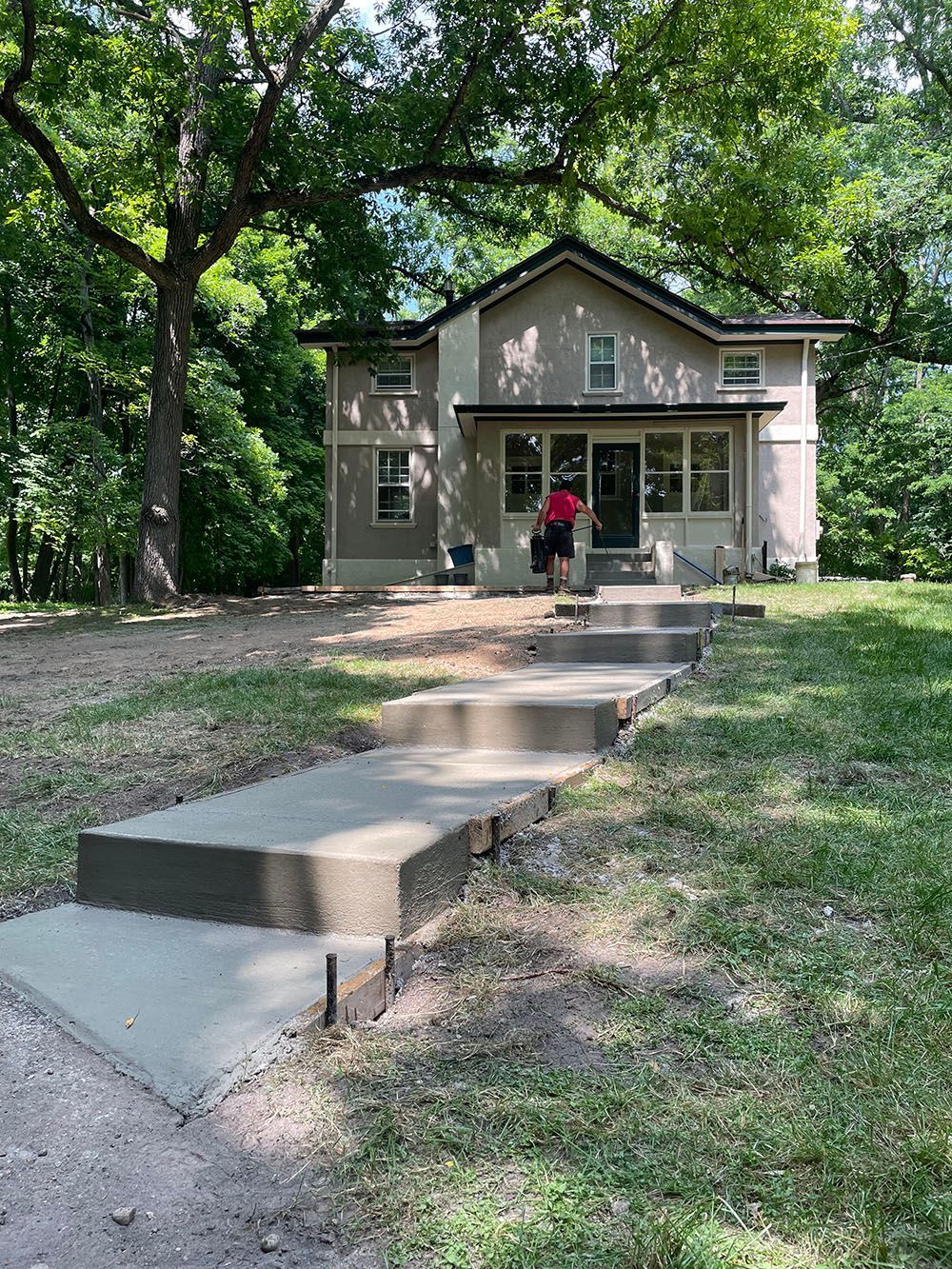 A man is standing in front of a house with a concrete walkway leading to it.