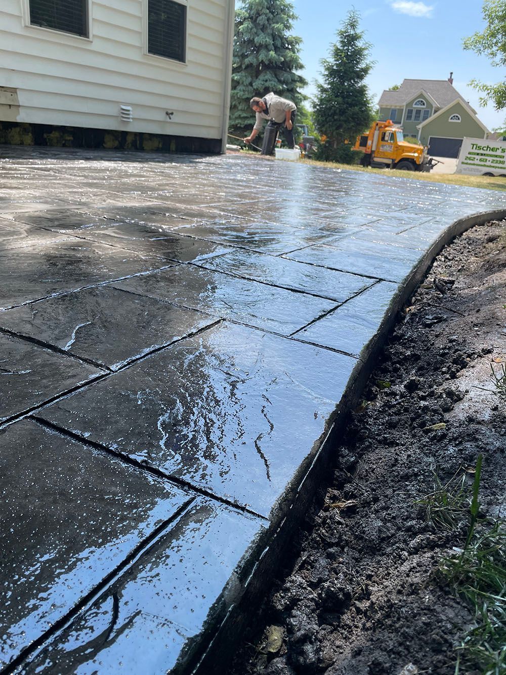 A man is working on a concrete driveway in front of a house.