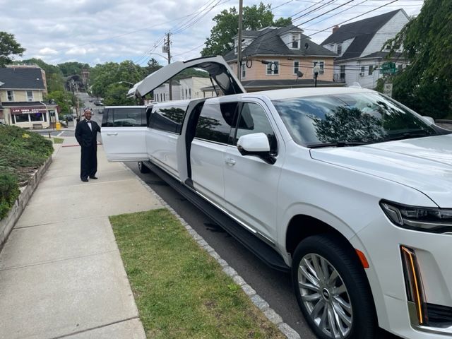 White limousine parked on a sidewalk, door open, person in black suit standing nearby.