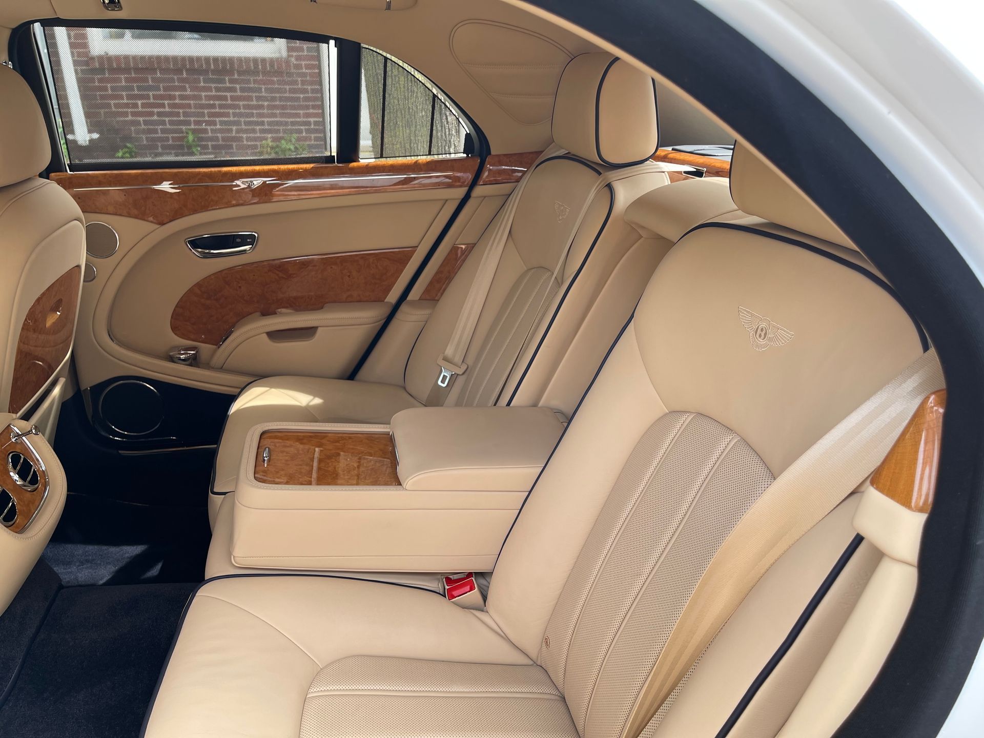 Beige leather Bentley backseat interior with wood paneling, featuring a center armrest and headrests.