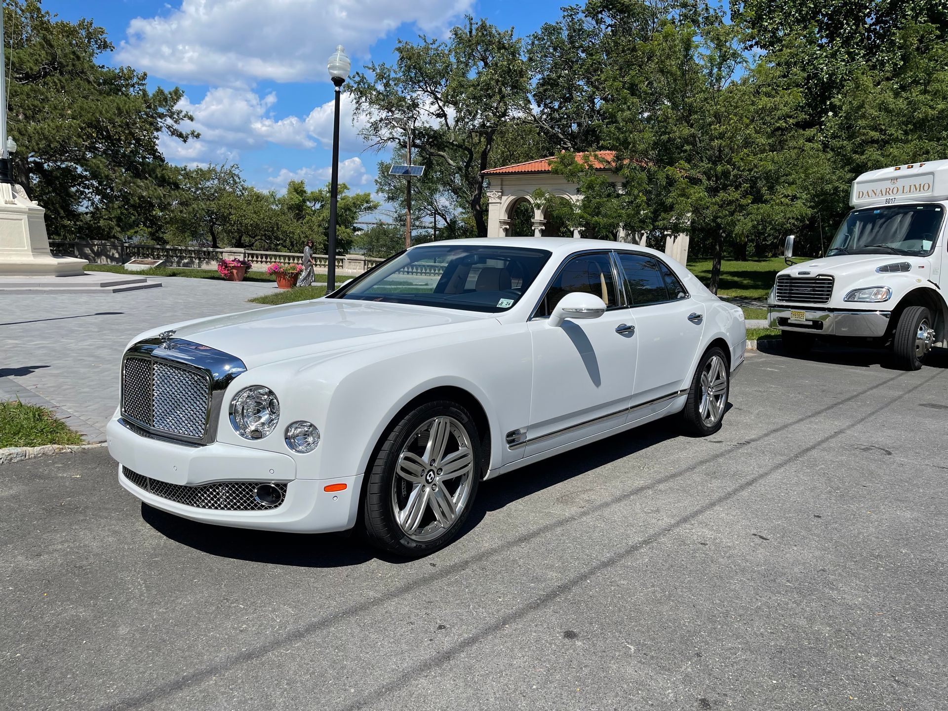 White Bentley sedan parked on pavement; trees and building in background.