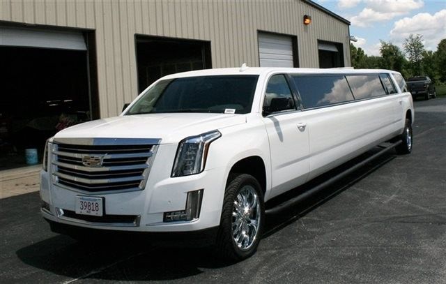 White Cadillac Escalade limousine parked in front of a building with garage doors.