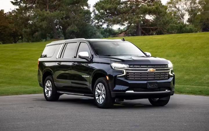 Black Chevrolet Suburban parked on a paved road with trees and grass in the background.
