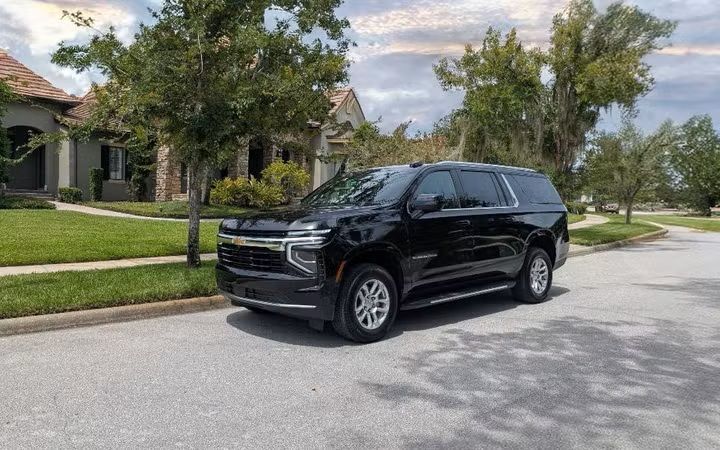 Black SUV parked on a suburban street in front of a house with a green lawn and trees.
