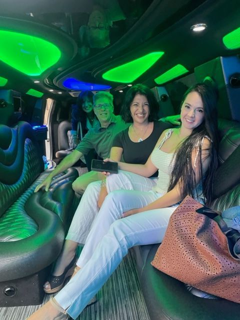 People in a limo with green lighting, smiling. Two women in white pants, one holding a bag. Man in green shirt.