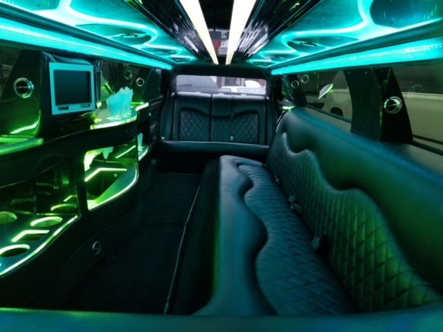 Interior of a limousine with teal and green lighting, leather seating, and a small TV screen.
